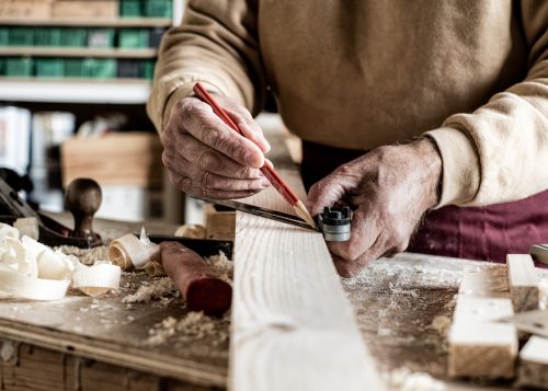 Carpenter making measurements with a pencil and a metal ruler on wooden plank